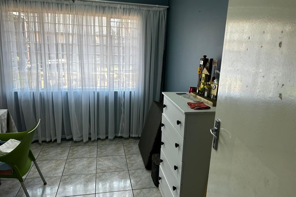 A bedroom featuring tiled flooring, a large window with curtains, and a neutral wall finish.