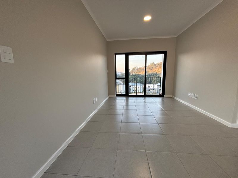 A bright, empty living area featuring neutral tiled flooring, recessed lighting, and a sliding glass door leading to a balcony with scenic views.