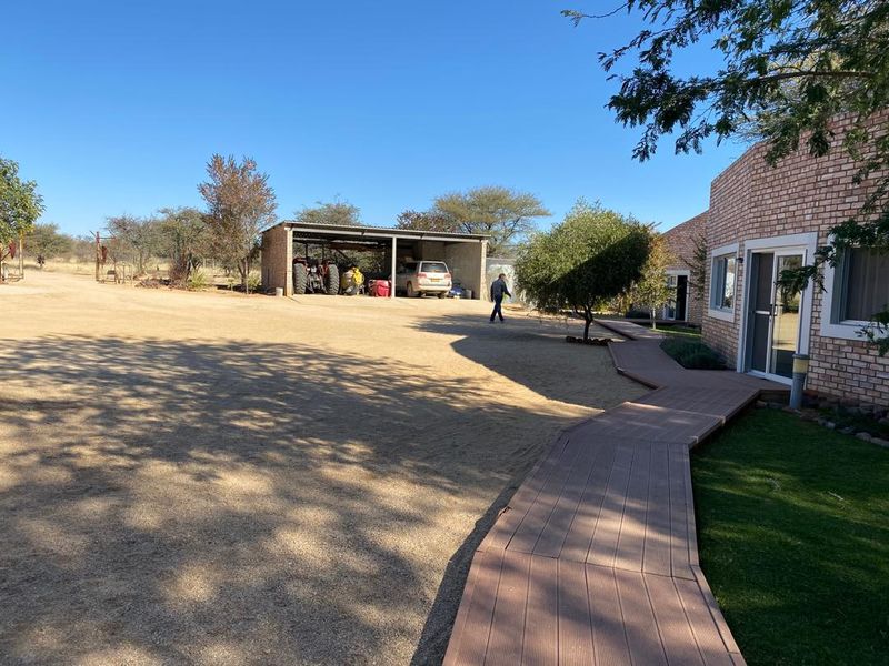 Exterior view of the farm property featuring a brick building, a composite decking walkway, and a detached open-sided garage structure.