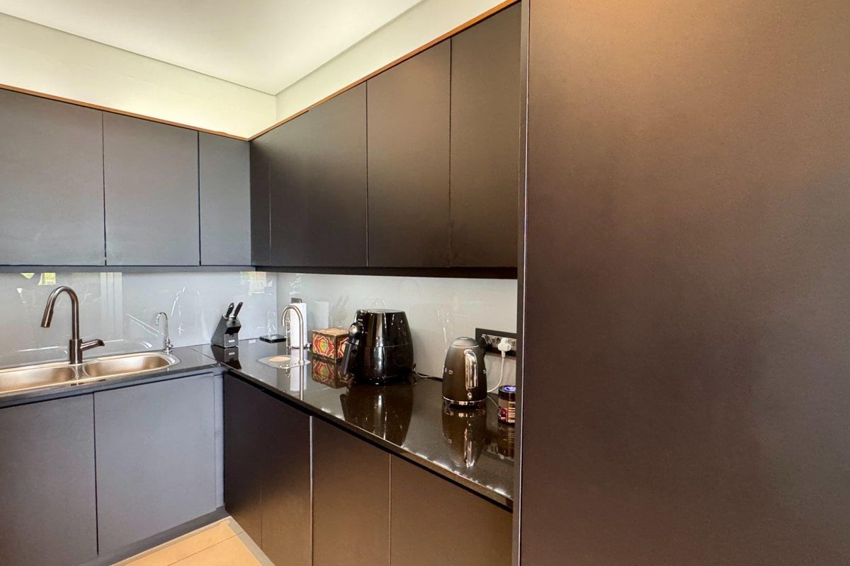 Modern kitchen featuring sleek dark cabinetry, polished stone countertops, a stainless steel double sink with a gooseneck mixer, and a clean glass splashback.