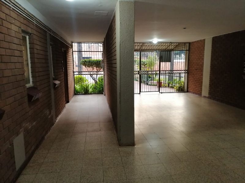 A spacious, covered entrance area featuring exposed brick walls, tiled flooring, and secure gated access to the exterior.
