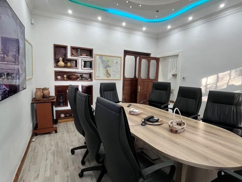 A professional office boardroom featuring a large oval table, recessed ceiling design with ambient LED lighting, and built-in wall shelving.