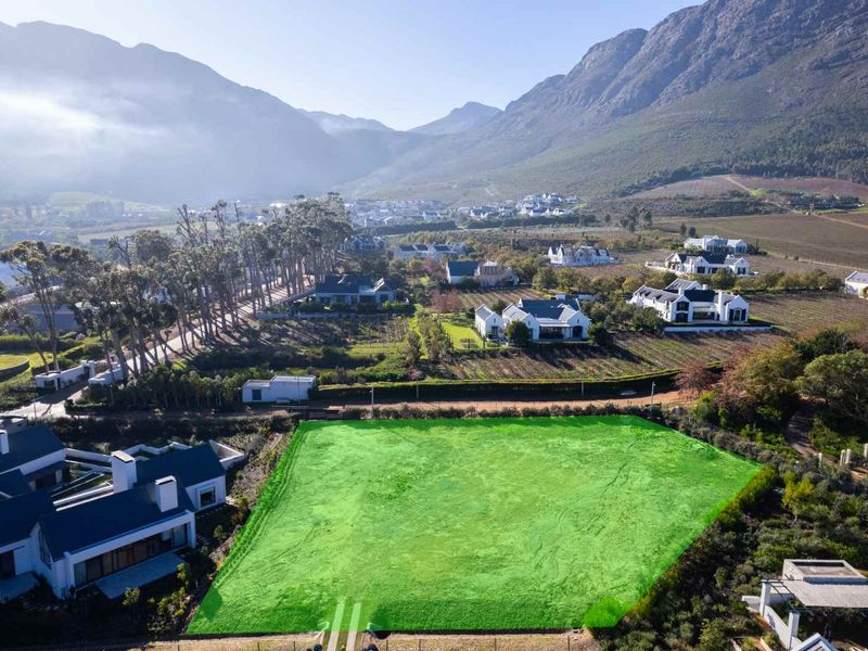 An aerial view of a vacant residential plot situated in a scenic estate with mountain views and surrounding established homes.
