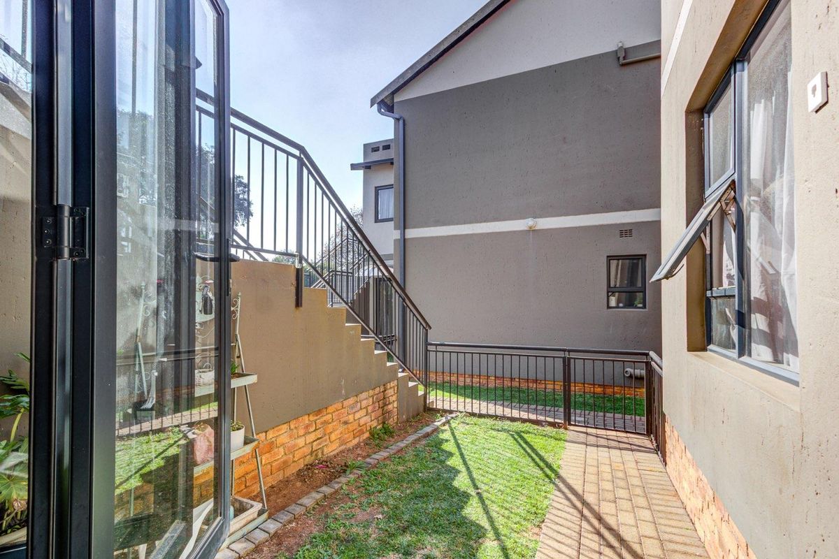 A side courtyard area featuring a paved walkway, small lawn, and external staircase with metal railings leading to an upper level.