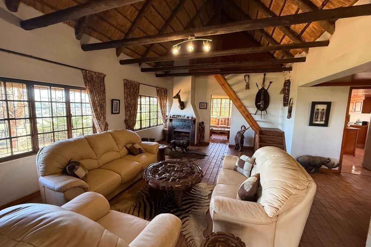 Spacious living room featuring a traditional thatched roof with exposed timber beams, terracotta tiled flooring, and a central fireplace.