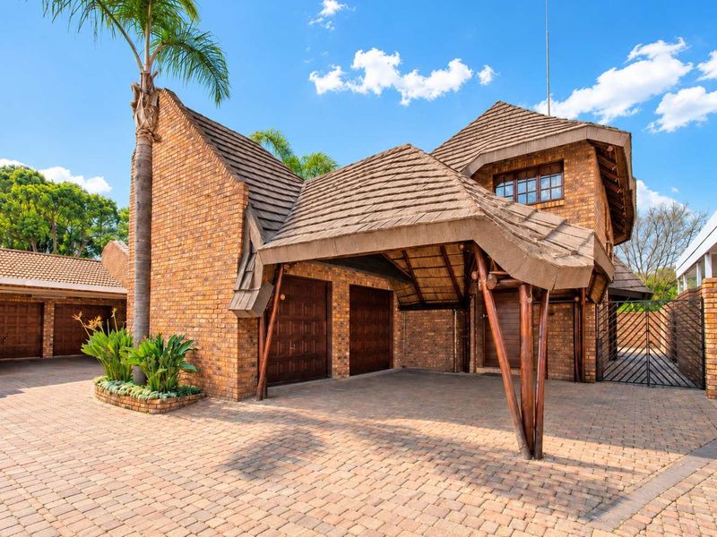 Front exterior view of a cluster property featuring a brick facade, double garage, paved driveway, and a unique thatched roof entrance structure.