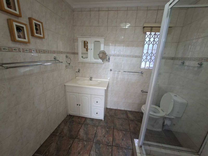 A functional bathroom featuring a vanity cabinet, shower enclosure, toilet, and tiled finishes throughout.