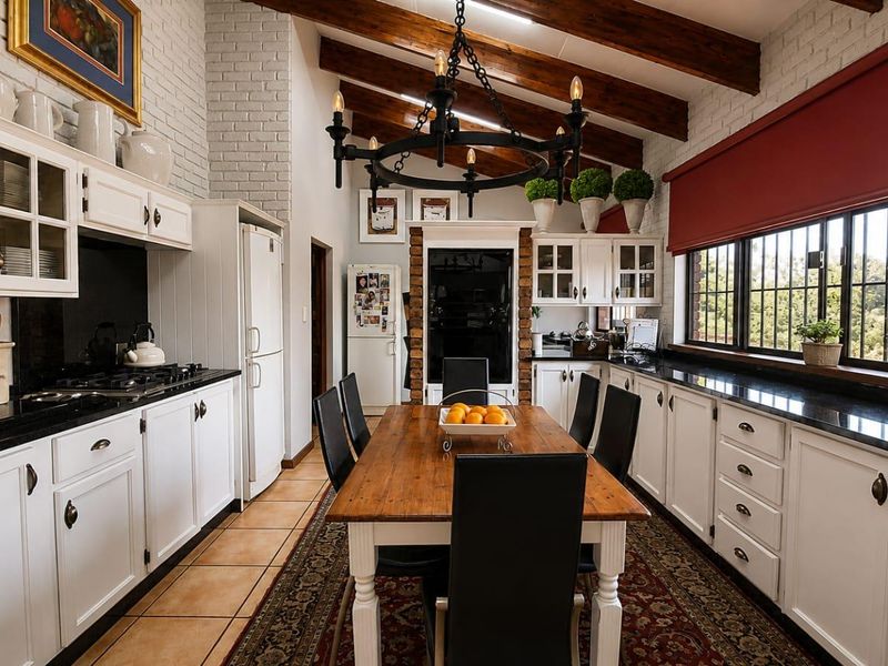 Spacious open-plan kitchen and dining area featuring exposed timber beams, painted brick walls, granite countertops, and a classic wrought iron chandelier.