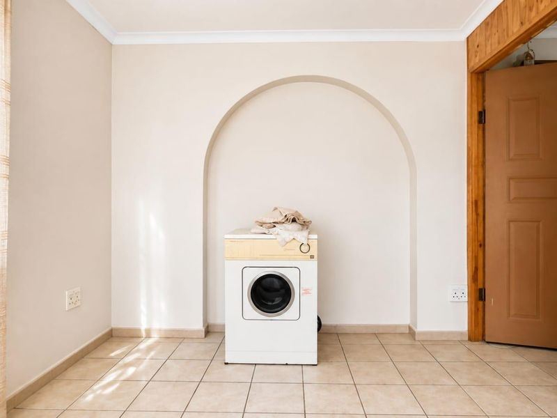 A functional laundry area featuring tiled flooring, a distinctive arched wall recess, and a timber door frame.