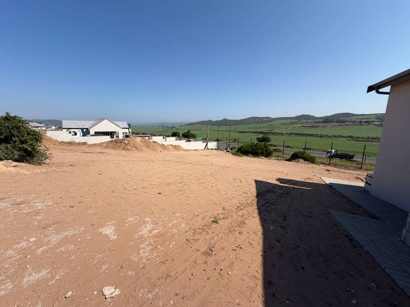 A view of the rear vacant land area featuring a paved walkway and perimeter fencing with surrounding landscape views.