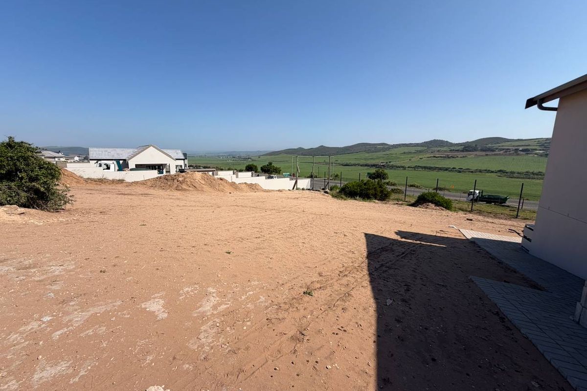 A view of the rear vacant land area featuring a paved walkway and perimeter fencing with surrounding landscape views.