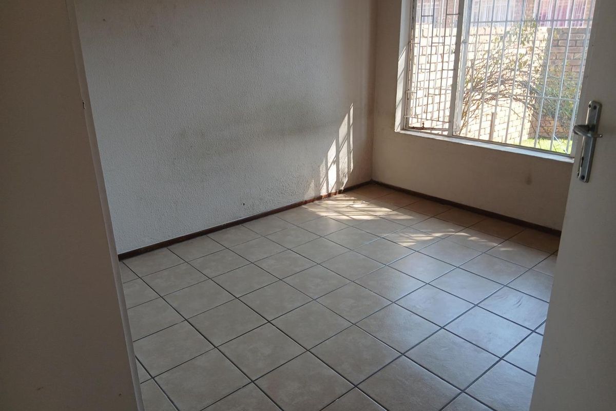 An empty bedroom featuring tiled flooring and a window fitted with security bars, offering a blank canvas for potential interior design.