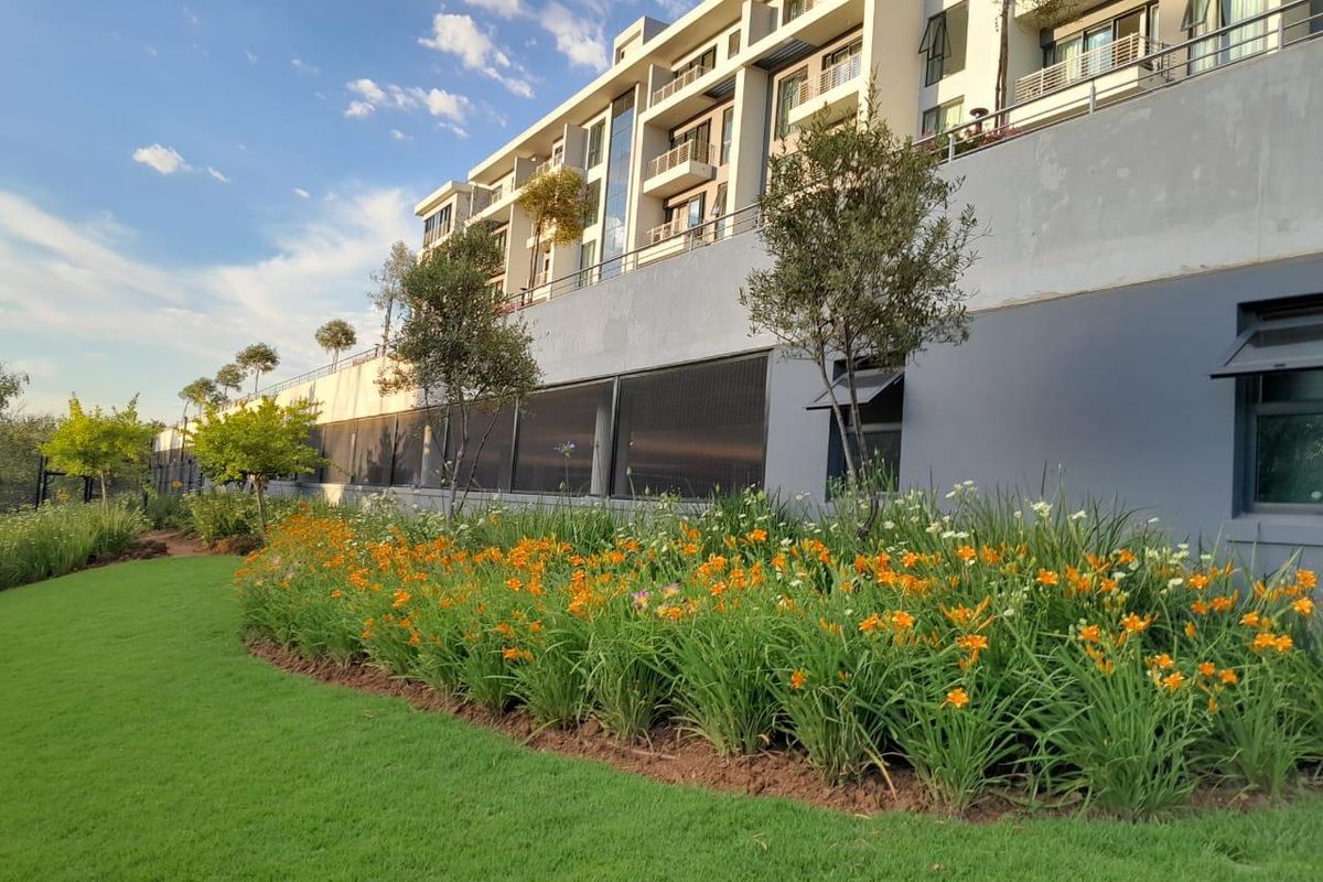 A well-maintained rear garden area featuring landscaped flower beds and lawn, set against the modern facade of an apartment building with private balconies.