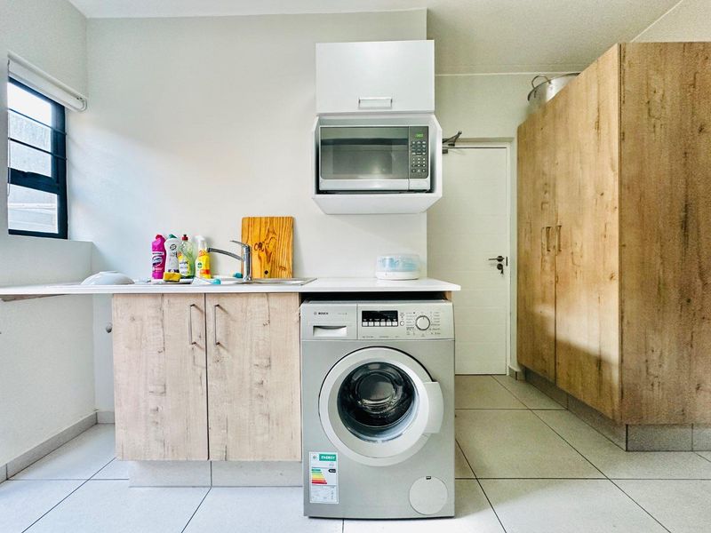 A functional laundry area featuring built-in cabinetry, a stainless steel sink, tiled flooring, and a built-in microwave with space for a washing machine.