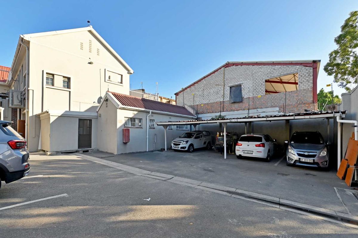 Exterior view of the property featuring a paved parking area with a covered carport structure and adjacent building elevations.