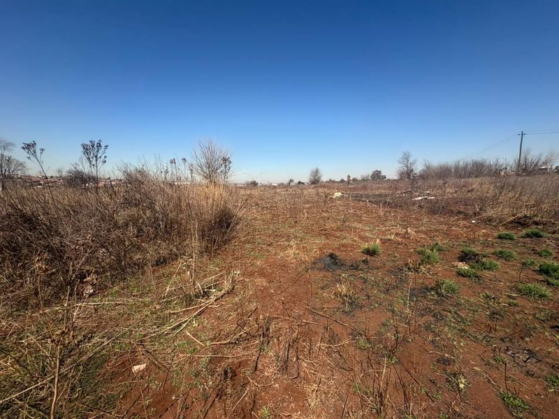 A wide-angle view of an undeveloped residential plot featuring dry, overgrown vegetation and natural terrain, suitable for future construction projects.