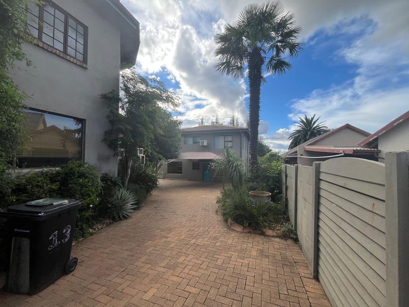 A paved driveway leading to the front of the property, featuring a precast boundary wall and established garden landscaping.
