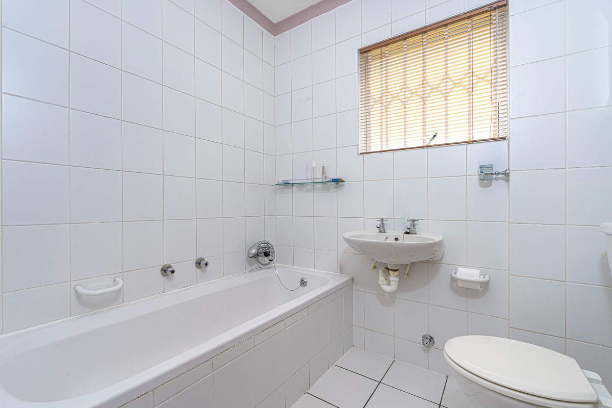 A functional bathroom featuring white wall and floor tiles, a standard bathtub, wall-mounted basin, and toilet.