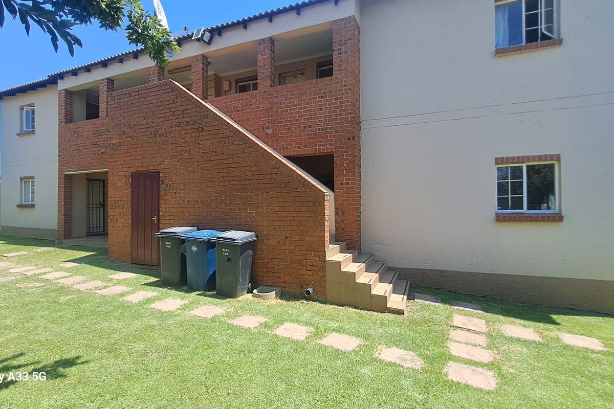 Rear view of a multi-story apartment building featuring exposed brickwork, an external staircase, and a shared garden area with paved stepping stones.