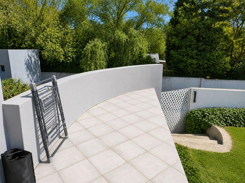 A clean, elevated patio area featuring a curved masonry wall, tiled flooring, and direct access to the garden via concrete steps.