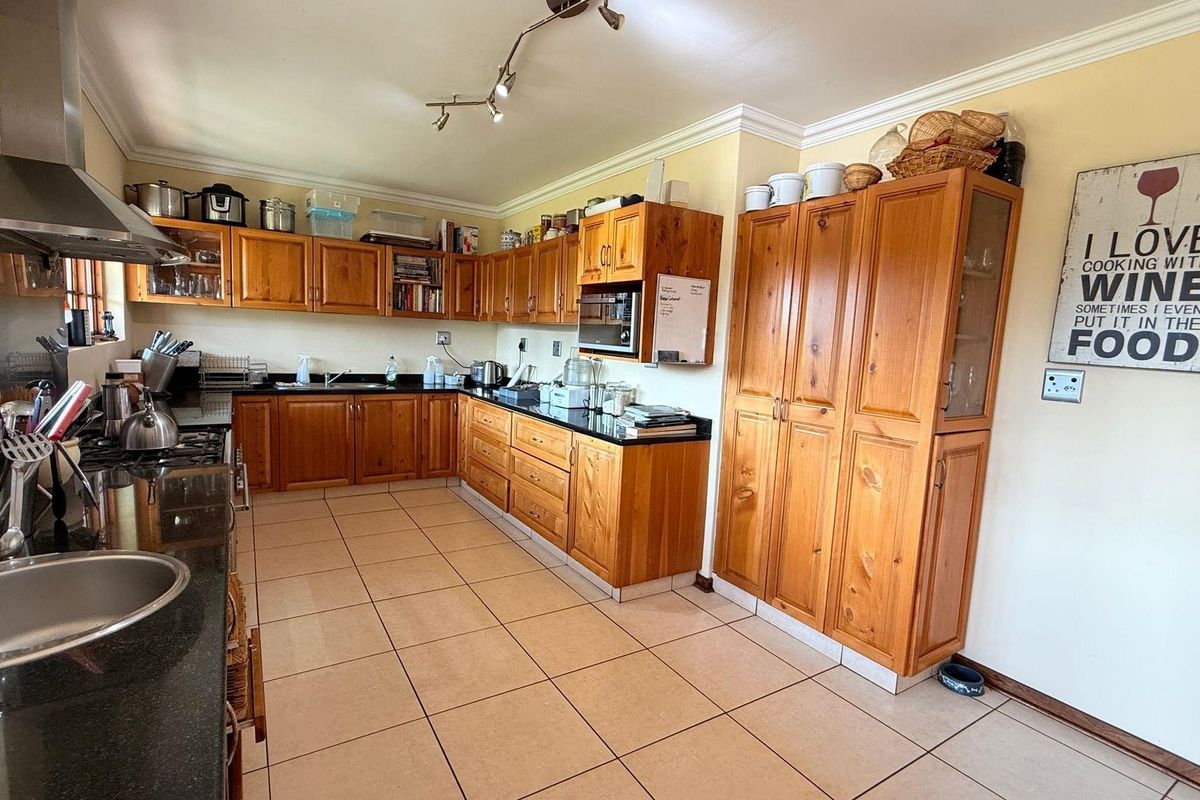 A functional kitchen featuring solid wood cabinetry, dark granite countertops, a stainless steel extractor fan, and tiled flooring.