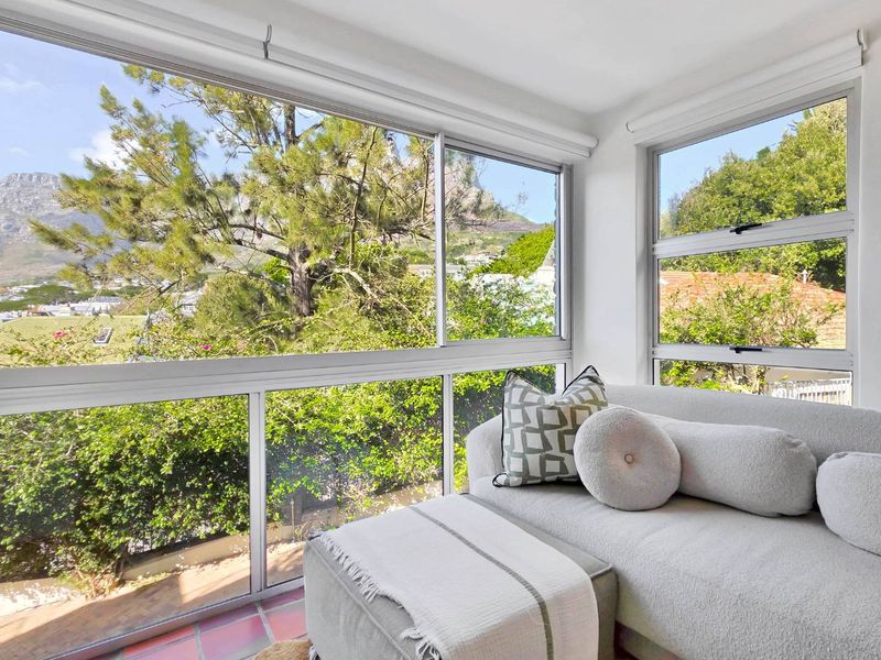 A bright, enclosed balcony featuring large sliding windows that offer scenic mountain and garden views, finished with tiled flooring and roller blinds.