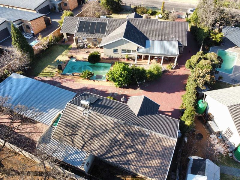 Aerial view of the property featuring a swimming pool, paved driveway, solar panels, and a covered patio area.