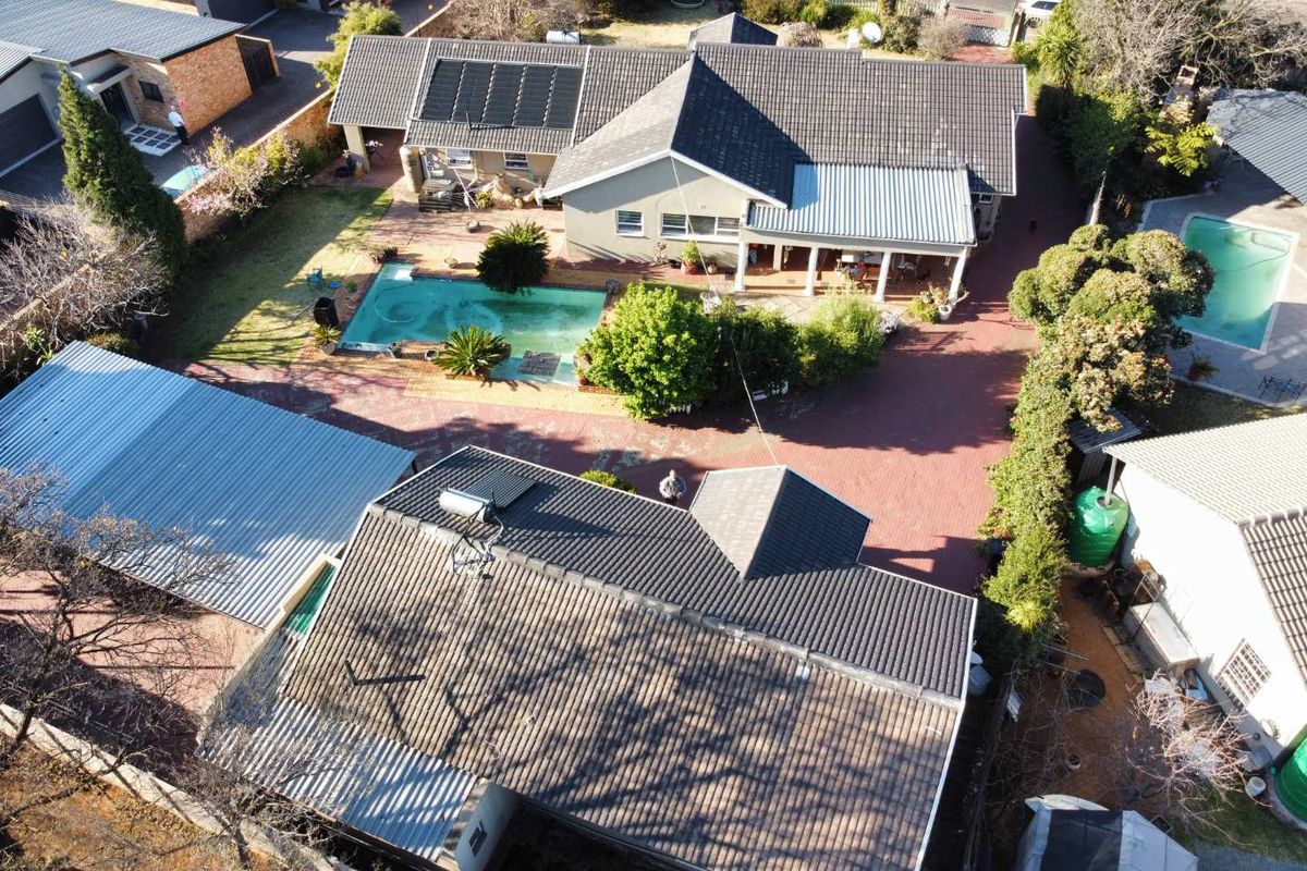 Aerial view of the property featuring a swimming pool, paved driveway, solar panels, and a covered patio area.