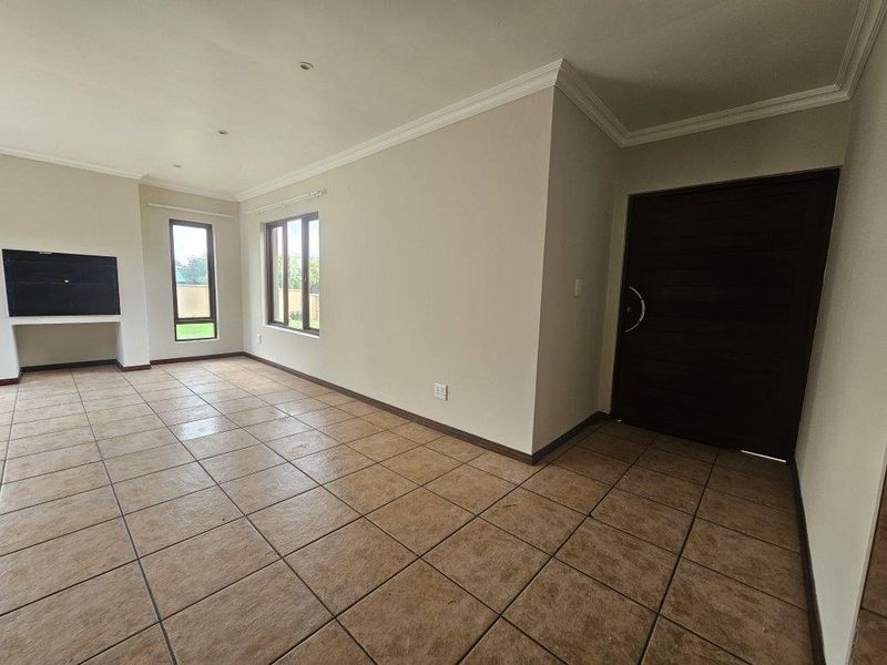 Spacious open-plan living area featuring neutral walls, tiled flooring, a built-in fireplace, and large windows providing ample natural light.