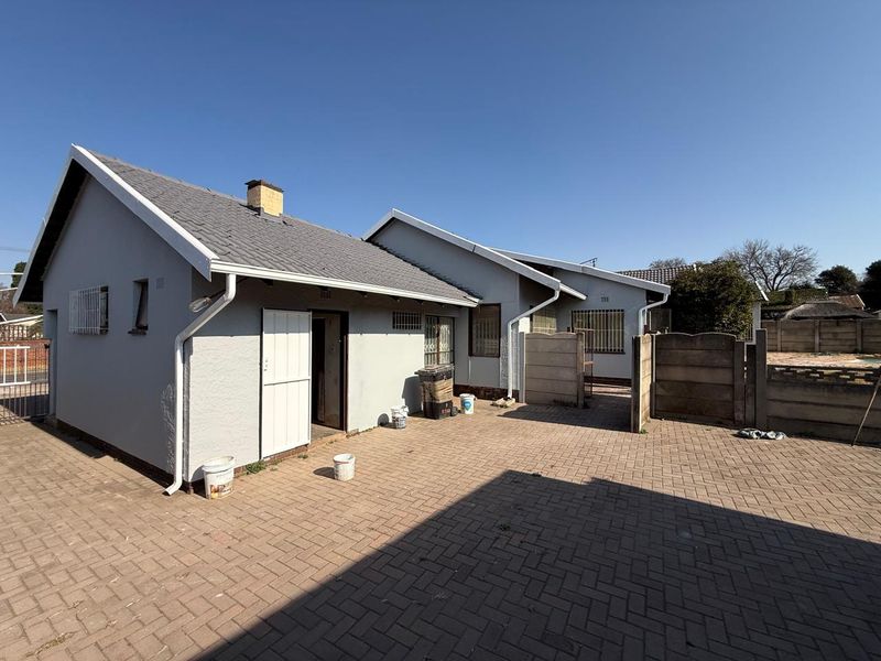 Rear view of the property featuring a paved courtyard, precast boundary walls, and a tiled roof structure with security bars on windows.