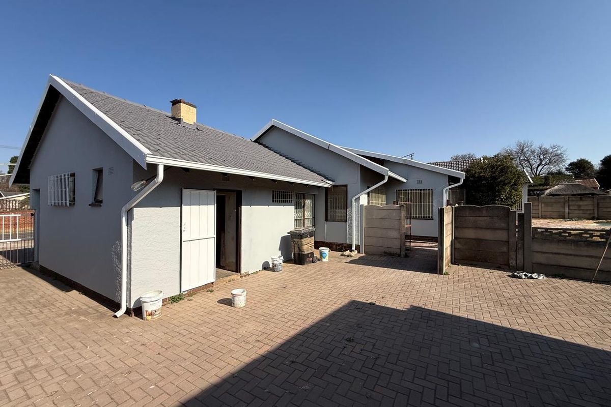 Rear view of the property featuring a paved courtyard, precast boundary walls, and a tiled roof structure with security bars on windows.