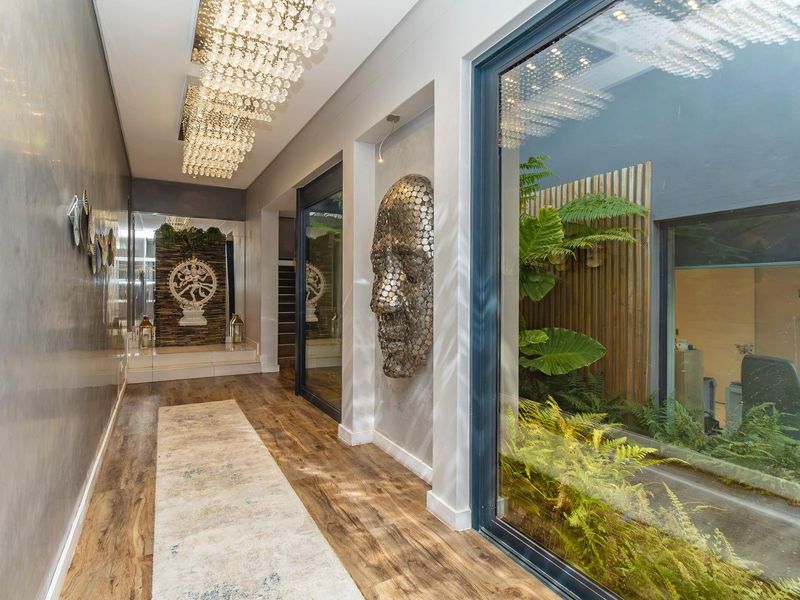 A modern, well-lit hallway featuring high-end finishes, decorative lighting, and a large glass wall overlooking a private internal courtyard garden.
