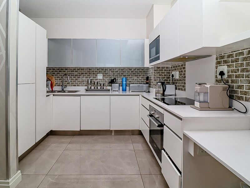 Modern kitchen featuring white cabinetry, stone countertops, tiled backsplash, and integrated appliances including an oven, hob, and microwave.