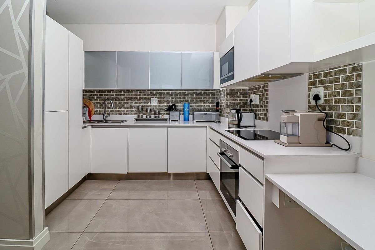Modern kitchen featuring white cabinetry, stone countertops, tiled backsplash, and integrated appliances including an oven, hob, and microwave.