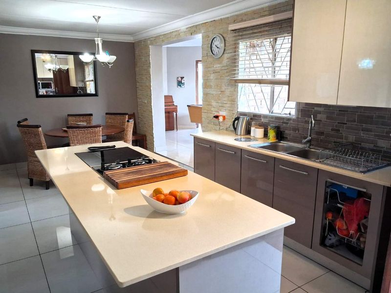 Modern open-plan kitchen featuring a central island with built-in hob, stone countertops, and sleek cabinetry, seamlessly flowing into the adjacent dining area.