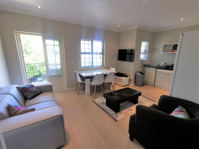 An open-plan living and kitchen area featuring light laminate flooring, recessed lighting, and direct access to a balcony through a glass door.