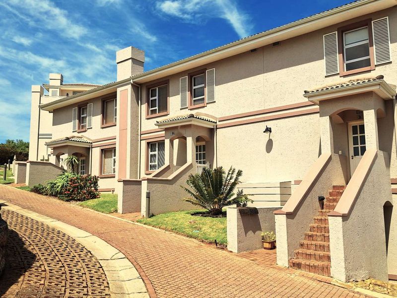 Front elevation of a townhouse complex featuring a brick paved driveway, stucco facade, and individual entrance steps with external lighting.