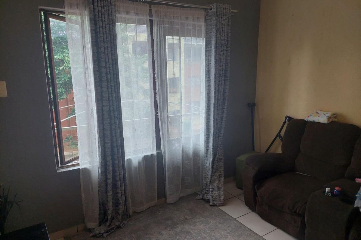 A living room area featuring tiled flooring and a large window with curtain fixtures, requiring minor cosmetic updates to the wall finishes.