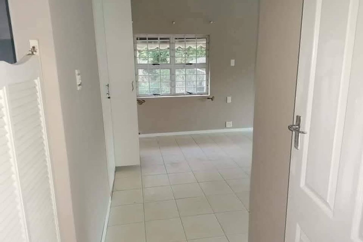 A vacant bedroom featuring neutral wall tones, tiled flooring, and built-in cupboard storage with security bars fitted to the window.