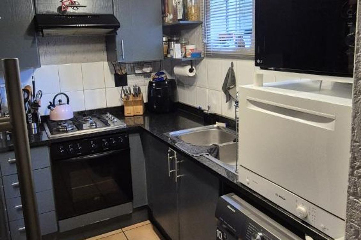 Compact kitchen featuring dark cabinetry, granite countertops, built-in oven, gas hob, extractor fan, and integrated laundry plumbing.