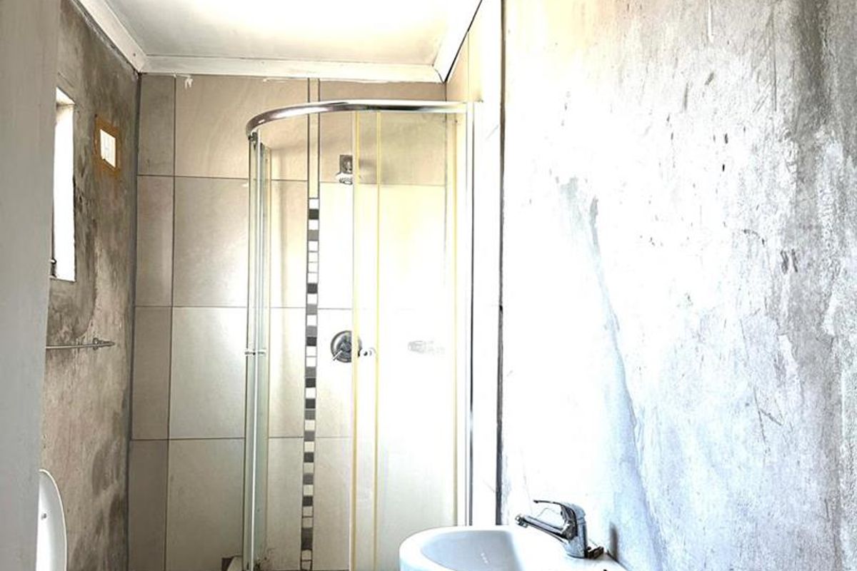A bathroom in need of renovation, featuring a pedestal basin, toilet, and corner shower enclosure with unfinished wall surfaces.