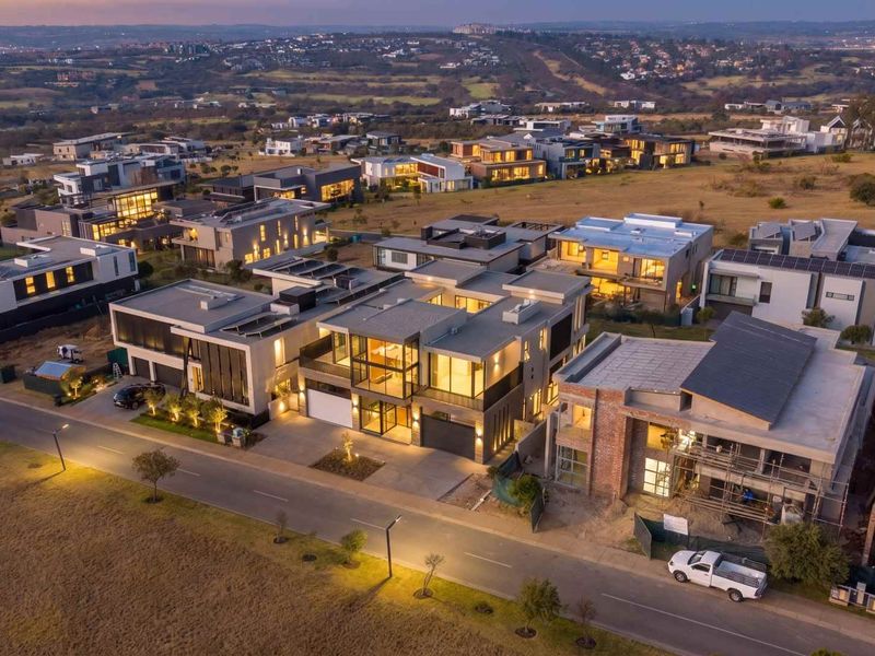 An aerial view of a modern residential estate at dusk, showcasing contemporary architectural designs, paved streets, and surrounding landscape.
