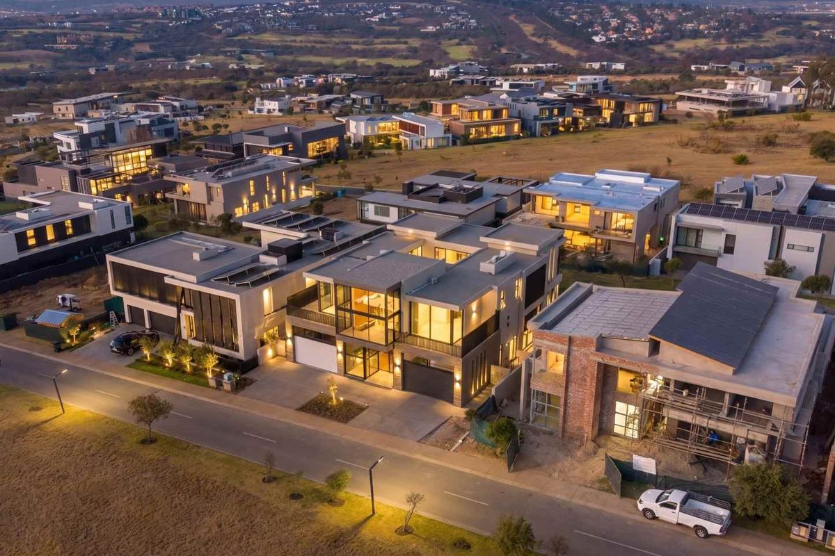 An aerial view of a modern residential estate at dusk, showcasing contemporary architectural designs, paved streets, and surrounding landscape.