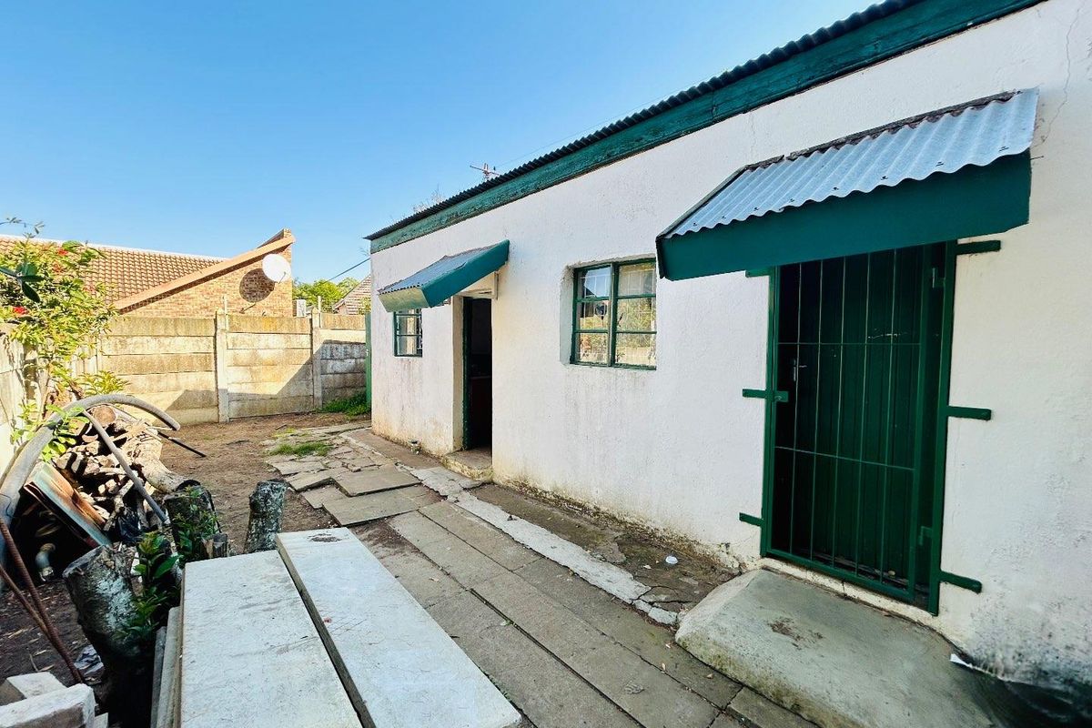 Rear exterior view of the property featuring a white rendered facade, green metal security gates, and a paved walkway leading to the entrance.