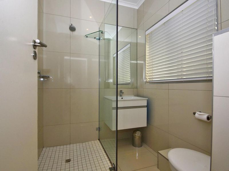 Modern bathroom featuring a walk-in shower with glass screen, wall-mounted vanity, and neutral floor-to-ceiling tiling.