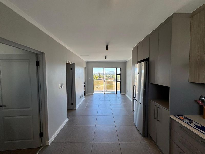 Modern open-plan living area featuring sleek built-in cabinetry, neutral tiled flooring, and direct access to a balcony with scenic views.