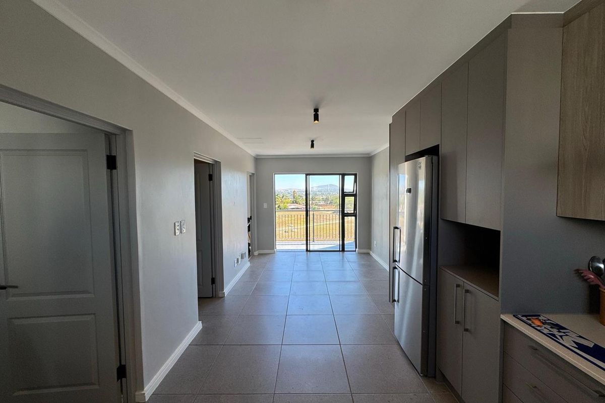 Modern open-plan living area featuring sleek built-in cabinetry, neutral tiled flooring, and direct access to a balcony with scenic views.
