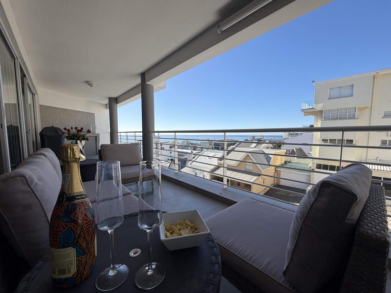 A spacious covered balcony featuring tiled flooring, a secure metal balustrade, and expansive urban and coastal views.