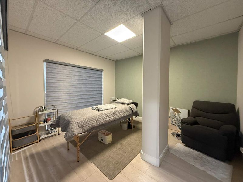 A functional office space featuring a suspended ceiling, recessed lighting, laminate flooring, and a central structural column with neutral wall finishes.