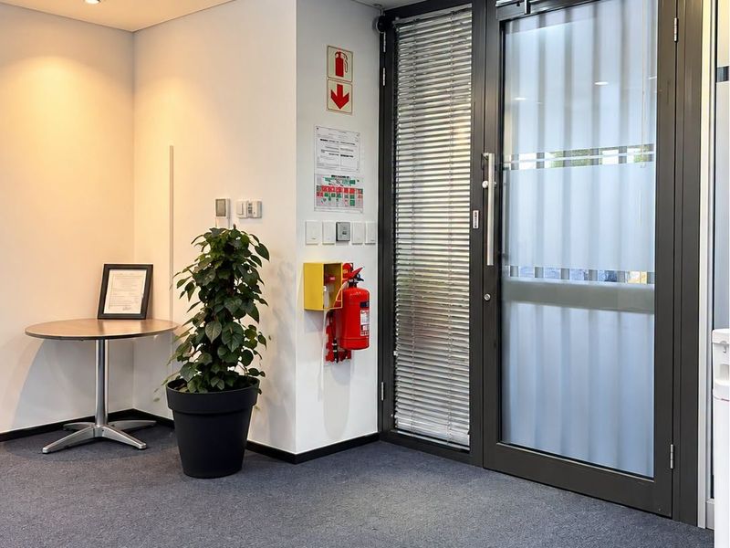 A clean and professional office entrance area featuring a glass door, carpeted flooring, and integrated fire safety equipment.